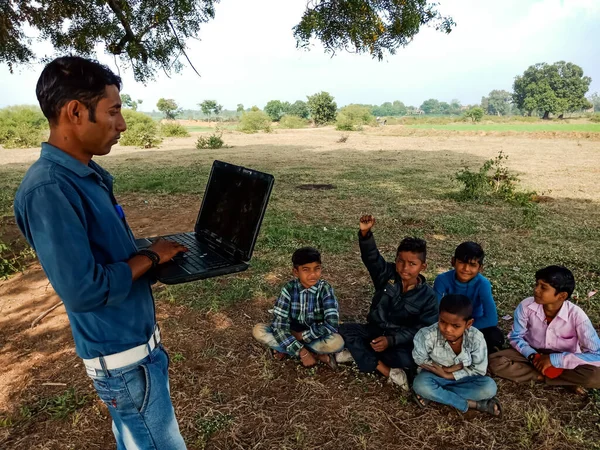 DISTRICT KATNI, INDIA - HAZİRAN 01, 2020: Bir Hintli şehir çocuğu açık alandaki fakir çocuklara dizüstü bilgisayar teknolojisi hakkında eğitim veriyor.