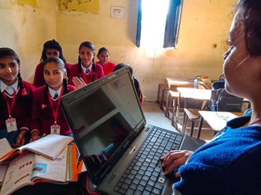 DİSTRİK KATNI, INDIA - 13 HAZİRAN 2020: Hintli ilkokul bayan öğretmeni sınıftaki öğrenciye laptop teknolojisi hakkında eğitim veriyor.