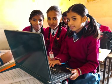 DİSTRİK KATNI, INDIA - 13 HAZİRAN 2020: Üç Hintli ilkokul kızı sınıf banklarında dizüstü bilgisayar teknolojisini birlikte öğreniyorlar.