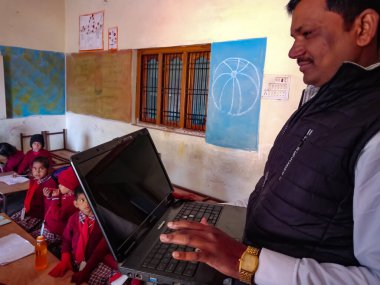 DİSTRİK KATNI, INDIA - 13 HAZİRAN 2020: Hintli erkek ilkokul öğretmeni sınıftaki öğrenciye laptop teknolojisi hakkında eğitim veriyor.