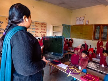 DİSTRİK KATNI, INDIA - 13 HAZİRAN 2020: Hintli ilkokul öğretmeni sınıftaki öğrenciye laptop teknolojisi hakkında eğitim veriyor.