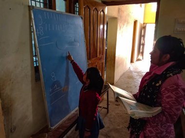 DİSTRİK KATNI, INDIA - 13 HAZİRAN 2020: Hintli ilkokul bayan öğretmeni sınıftaki küçük kız öğrenciye gemide yazma eğitimi veriyor.