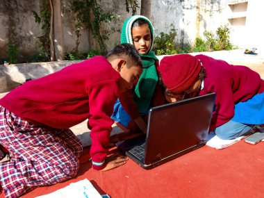 DISTRICT KATNI, INDIA - 13 HAZİRAN 2020: Açık alanda dizüstü bilgisayar teknolojisini birlikte öğrenen üç Hintli ilkokul öğrencisi.