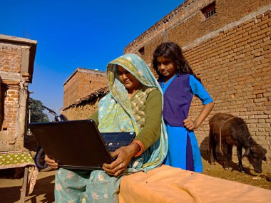 DISTRICT KATNI, INDIA - 25 Ocak 2020: Mavi gökyüzü arka planında torunuyla dizüstü bilgisayarı öğrenen Hintli bir kadın.