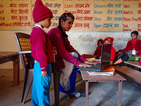 DİSTRİK KATNI, INDIA - 13 HAZİRAN 2020: Hintli ilkokul bayan bilgisayar öğretmeni sınıftaki erkek öğrenciye laptop teknolojisi hakkında eğitim veriyor.