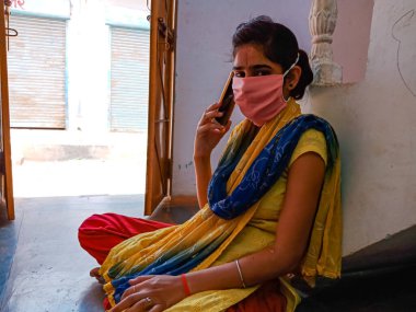 DISTRICT KATNI, INDIA - 21 Mayıs 2020: Evde Coronavirus koruması için yüz maskesi takan Hintli bir kız cep telefonundan arıyor.