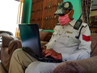 DISTRICT KATNI, INDIA - 21 Mayıs 2020: Evde dizüstü bilgisayarda çalışan Hintli bir polis Coronavirus koruması için maske takıyor.