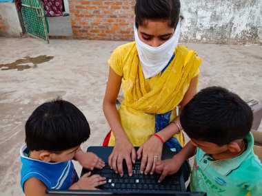 DISTRICT KATNI, INDIA - 23 Mayıs 2020: Korona virüs koruması için yüz maskesi takan küçük çocuklara dizüstü bilgisayar teknolojisi eğitimi veren Hintli bir kız.