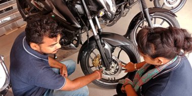 DISTRICT KATNI, INDIA - 21 Eylül 2019: Motorsiklet Bajaj bayiliğinde iki Hintli otomobil satış görevlisi motorsiklet tekerleği gösterisi.