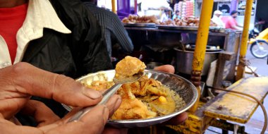 DISTRICT KATNI, INDIA - 24 EYLÜL 2019: Market caddesindeki sokak yemekleri dükkanında kaşıkla samosa yiyen Hintli bir adam.