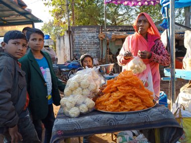 DISTRICT KATNI, INDIA - Şubat 02, 2020: Hint köyü kadını Hintçe Jalebi adı verilen geleneksel tatlıyı köy pazarı sezonu sırasında at arabası dükkanındaki çocuklara satıyor.