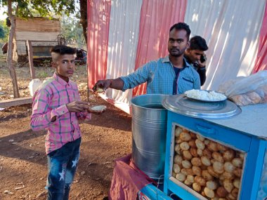 DISTRICT KATNI, INDIA - Şubat 02, 2020: köy pazarı festivali sezonu sırasında at arabası dükkanındaki çocuğa panipuri veren Hintli bir adam.