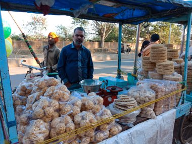DISTRICT KATNI, INDIA - Şubat 02, 2020: Köy pazarı festivali sezonu sırasında at arabası dükkanındaki müşterilere geleneksel tatlı satan bir Asyalı.