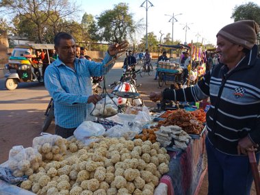 DISTRICT KATNI, INDIA - Şubat 02, 2020: Köy pazarı festivali sezonu sırasında bir Asyalı köylü at arabası dükkanındaki müşteriye geleneksel şeker satıyor.