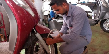DISTRICT KATNI, INDIA - 15 Eylül 2019: Hintli otomobil atölyesinde motosiklet lastiği ile hava dolduran Asyalı bir motosiklet servis işçisi.