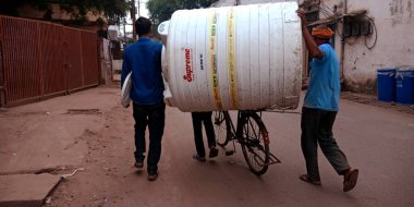 DISTRICT KATNI, INDIA - 06 Ekim 2019: İki Hintli insan bisiklet üzerinde en yüksek plastik su tankını taşıyorlar.