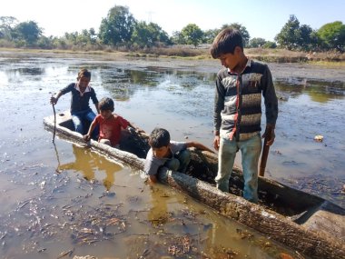 DISTRICT KATNI, INDIA - HAZİRAN 01, 2020: Bir grup fakir köy çocuğu doğal ortamda gölde tekneyle geziyorlar.
