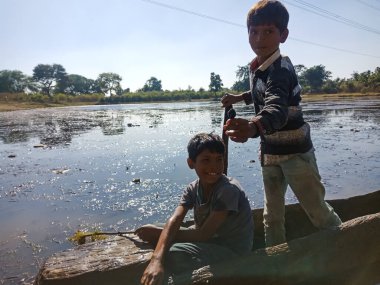 DİSTRİK KATNI, INDIA - HAZİRAN 01, 2020: İki Asyalı köy çocuğu doğal ortamda gölde tekneyle geziyorlar.