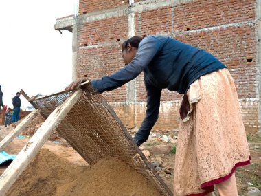 DİSTRİK KATNI, Hindistan - 18 Aralık 2019: Yerli bir köylü işçi kız gökyüzü arka planındaki ev inşaatındaki kumu filtreliyor.