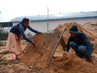 DİSTRİK KATNI, INDIA - 18 Aralık 2019: Gökyüzü arka planındaki ev inşaatındaki kumu filtreleyen iki Hint köyü işçisi.