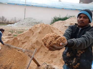 DİSTRİK KATNI, INDIA - 18 Aralık 2019: Bir Hint köyü erkek işçisinin ev inşaatındaki fotoğraf için kameraya kum sunması.