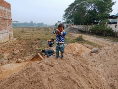 DISTRICT KATNI, INDIA - 18 Aralık 2019: İnşaat alanında kum deposunda oynayan küçük bir Hint köyü çocuğu.