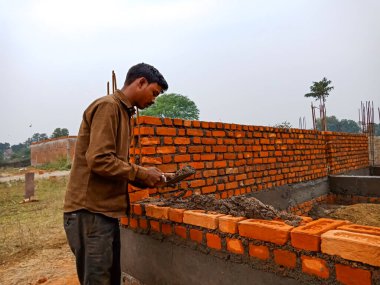 DISTRICT KATNI, INDIA - 18 Aralık 2019: Asyalı bir köy inşaat işçisi inşaat sahasında tuğla duvar oluşturmak için betonlaşmış materyal uyguluyor.