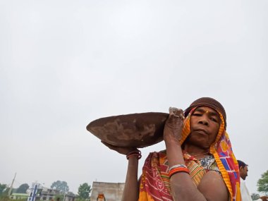 DISTRICT KATNI, INDIA - 18 ARALIK 2019: Hindistan 'ın yaşlı kadın işçi köyü gökyüzü arka planındaki inşaat alanında inşaat malzemeleri taşıyor.