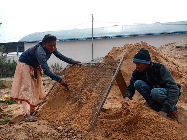 DİSTRİK KATNI, INDIA - 18 Aralık 2019: Gökyüzü arka planındaki ev inşaatındaki kumu filtreleyen iki Hint köyü işçisi.
