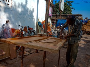 DISTRICT KATNI, Hindistan - 08 Ocak 2020: Asyalı yaşlı bir marangoz açık alan atölyesinde ahşap kapı yapıyor.