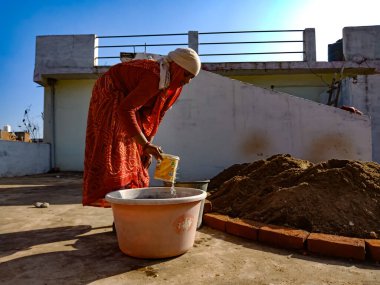 DİSTRİK KATNI, INDIA - 13 Ocak 2020: Gökyüzü duvarı arka planında inşaat alanında malzeme karıştırmak için su toplayan Hintli bir kadın işçi.