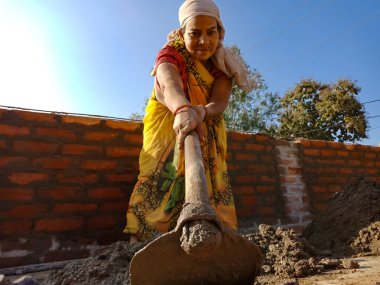 DISTRICT KATNI, INDIA - 13 Ocak 2020: Hintli bir kadın işçilik, gökyüzü duvarı arka planındaki inşaat sahasında maça aletinden elle yapı malzemelerini karıştırıyor.