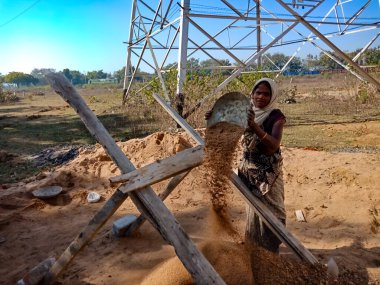 DISTRICT KATNI, INDIA - 18 HAZİRAN 2020: Gökyüzü arka planındaki inşaat alanında kumları filtreleyen Hintli bir köylü kadın işçi.