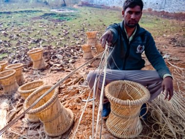 DISTRICT KATNI, INDIA - 18 HAZİRAN 2020: Asyalı bir köylü, doğal arka plandaki açık alan atölyesinde sandalye gösterisi için kuru ot sunuyor.