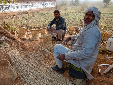 DISTRICT KATNI, INDIA - 18 HAZİRAN 2020: Kuru ot yapan iki Hintli köy işçisi, doğal arka plandaki açık alan atölyesinde ev dekorasyonu yaptı.