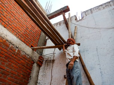 DISTRICT KATNI, INDIA - 18 HAZİRAN 2020: Tuğla duvar arka planındaki inşaat alanında duvar desteği için bambu ahşap yapısını bağlayan bir Hint köyü erkek işçiliği.