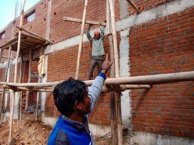 DISTRICT KATNI, INDIA - 18 HAZİRAN 2020: Tuğla duvar arka planındaki inşaat alanında duvar desteği için bambu ahşap yapısını işaret eden bir Hint köyü işçiliği.