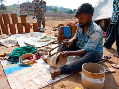 DISTRICT KATNI, INDIA - 21 HAZİRAN 2020: Hintli yoksul köylü sanatçı açık alan atölyesindeki toprak sahada elle trampet tabanını kesiyor.