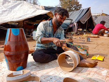 DISTRICT KATNI, INDIA - 21 HAZİRAN 2020: Hintli yoksul köylü sanatçı açık alan atölyesindeki toprak sahada elle trampet tabanını kesiyor.