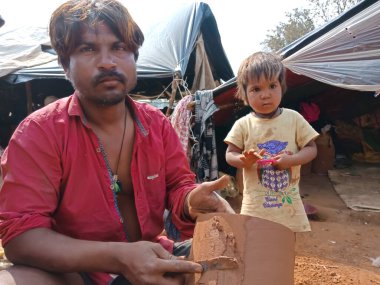 DISTRICT KATNI, INDIA - 21 HAZİRAN 2020: Hintli fakir erkek sanatçı açık alan atölyesindeki toprak alanında çocukla birlikte davul tabanına toprak uyguluyor.