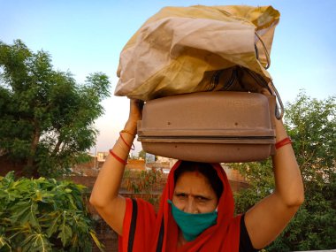 DISTRICT KATNI, INDIA - 21 Mayıs 2020: Corona virüsü koruması için yüz maskesi takan Hintli bir köylü kadın, gökyüzü arka planında kafasında aksesuar sakladı.