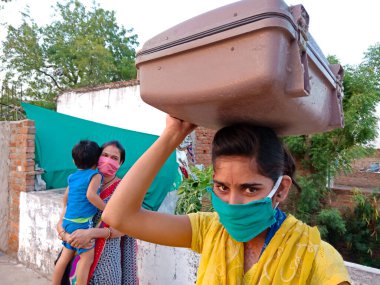 DISTRICT KATNI, INDIA - 21 Mayıs 2020: Corona virüsü koruması için yüz maskesi takan Hintli fakir bir kız gökyüzü arka planında kafasının üzerinde aksesuar sakladı.