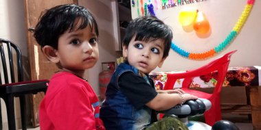 DİSTRİK KATNI, INDIA - 2 HAZİRAN 2020: 2 Hintli şirin çocuk evde oyuncak bisiklette yan yana oturuyorlar.