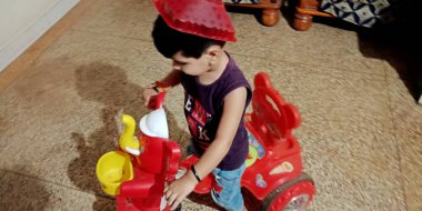 DİSTRİK KATNI, INDIA - 10 HAZİRAN 2020: Evinde oyuncak bisiklete binen Asyalı küçük bir çocuk, korunmak için komik bir kask takıyor..