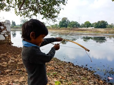 DISTRICT KATNI, INDIA - HAZİRAN 01, 2020: Asyalı köy çocuğu nehir kıyısındaki su gölüne ok doğrultuyor.