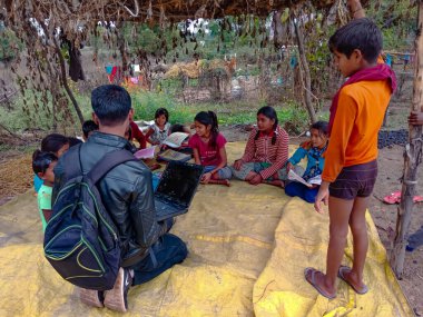 DISTRICT KATNI, INDIA - HAZİRAN 01, 2020: Bir Hintli şehir çocuğu köy açık hava ortamında birlikte fakir çocuklara dizüstü bilgisayar eğitimi hakkında eğitim veriyor.