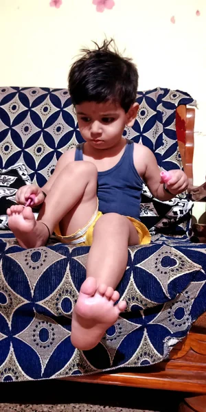DİSTRİK KATNI, INDIA - 12 HAZİRAN 2020: Evde ayak tırnaklarına oje süren Hintli küçük sevimli bir erkek çocuk.