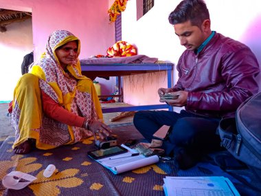 DISTRICT KATNI, INDIA - 16 HAZİRAN 2020: Köydeki yaşlı kadın evdeki küçük mikro finansman geri ödeme prosedürü sırasında elektronik başparmak pedi makinesine dokunuyor.