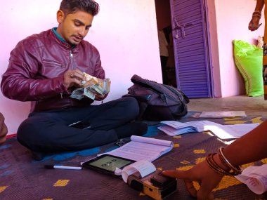 DISTRICT KATNI, INDIA - 16 HAZİRAN 2020: Küçük banka memurunun önündeki elektronik başparmak izi makinesine dokunan kadın, evdeki küçük mikro finansman kredi geri ödeme prosedürü sırasında.