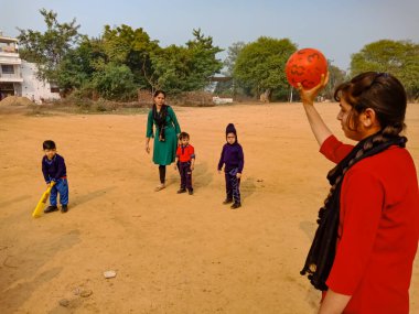DISTRICT KATNI, INDIA - 17 HAZİRAN 2020: Hint anaokulu bayan öğretmeni spor sahasında kriket oynarken top atıyor.
